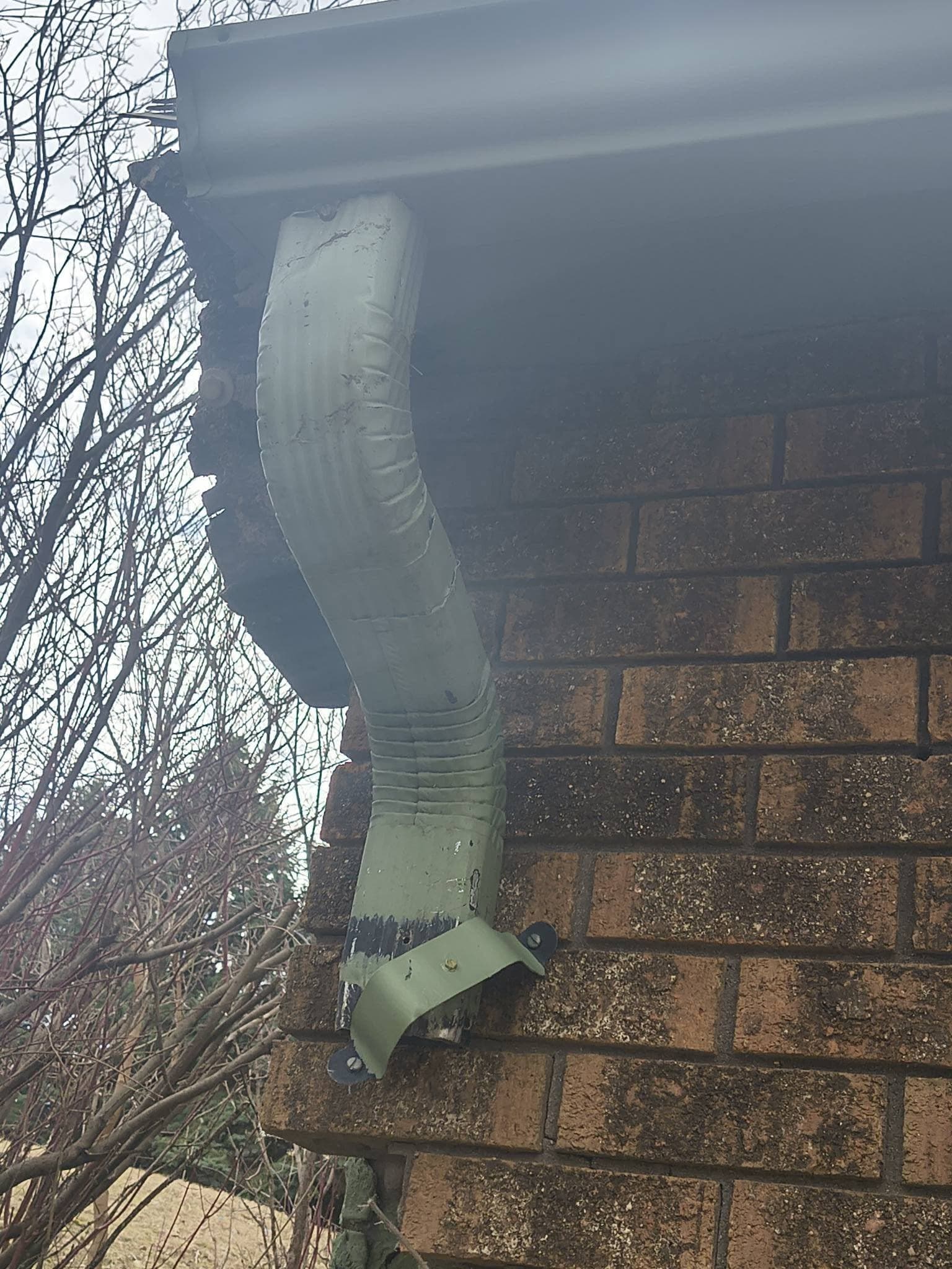An old downspout elbow crushed nearly flat against a brick wall