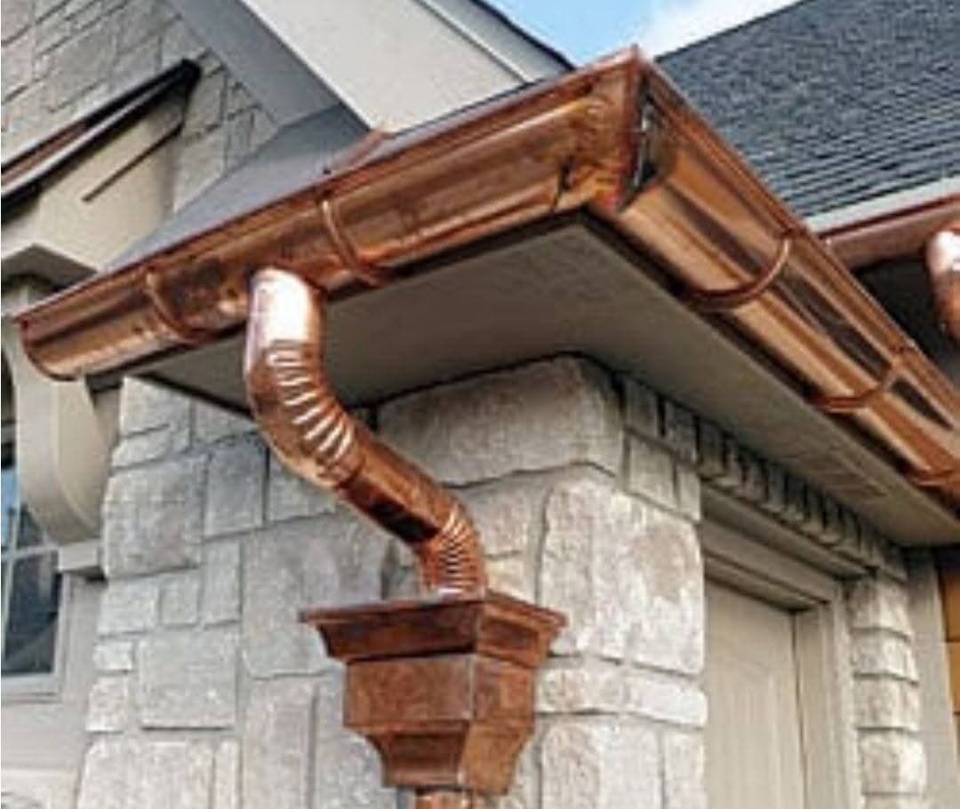 Copper gutter with a decorative collector box and curved copper downspout on a stone exterior