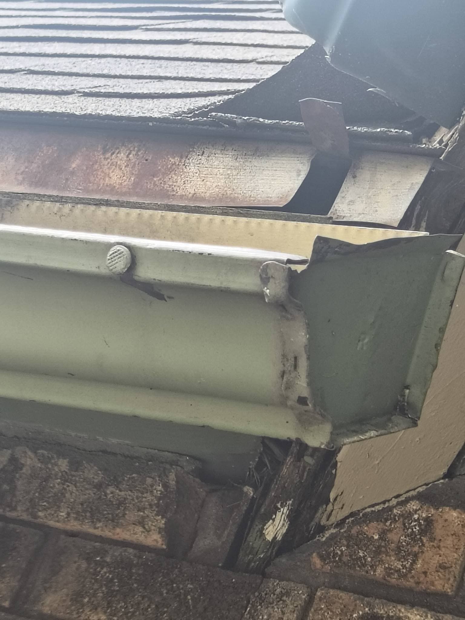 An old gutter corner separated from rusted drip edge with rotted fascia board behind it