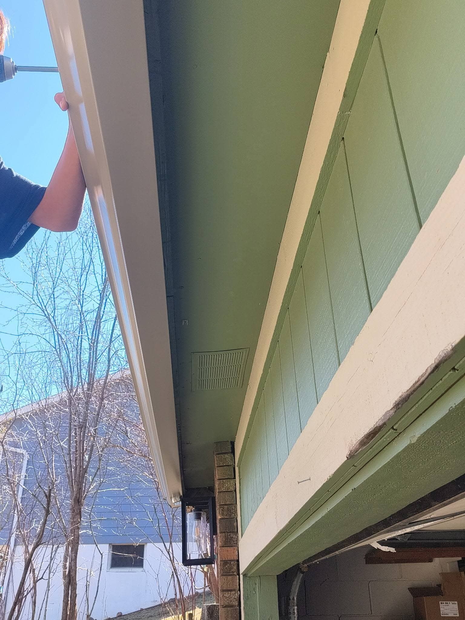 Installer's hands guiding a new white gutter run onto the fascia, seen from below