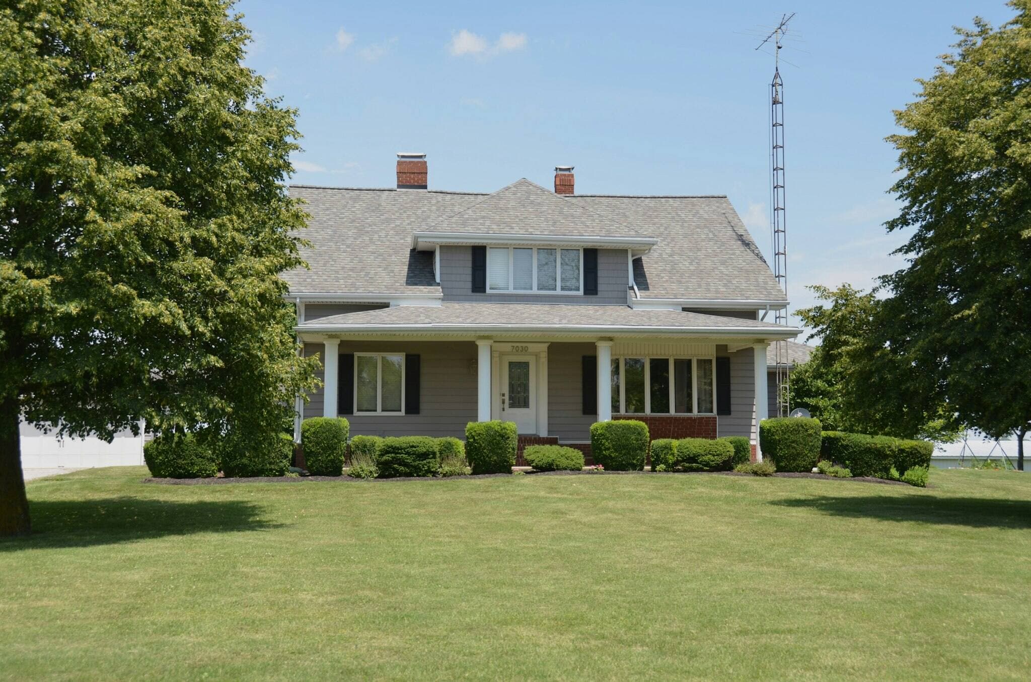 Illustrative wide view of a two-story gray house with clean white eave and gutter lines on a mowed lawn