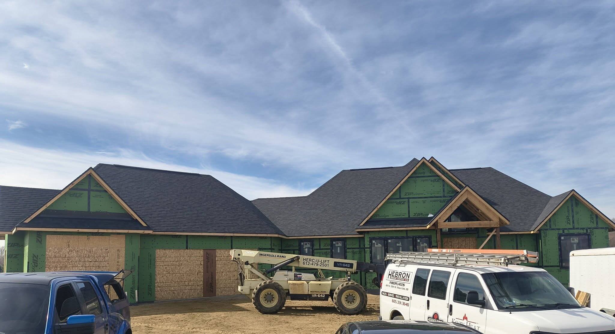 Wide view of a large lodge-style new build with work trucks and a lift on site