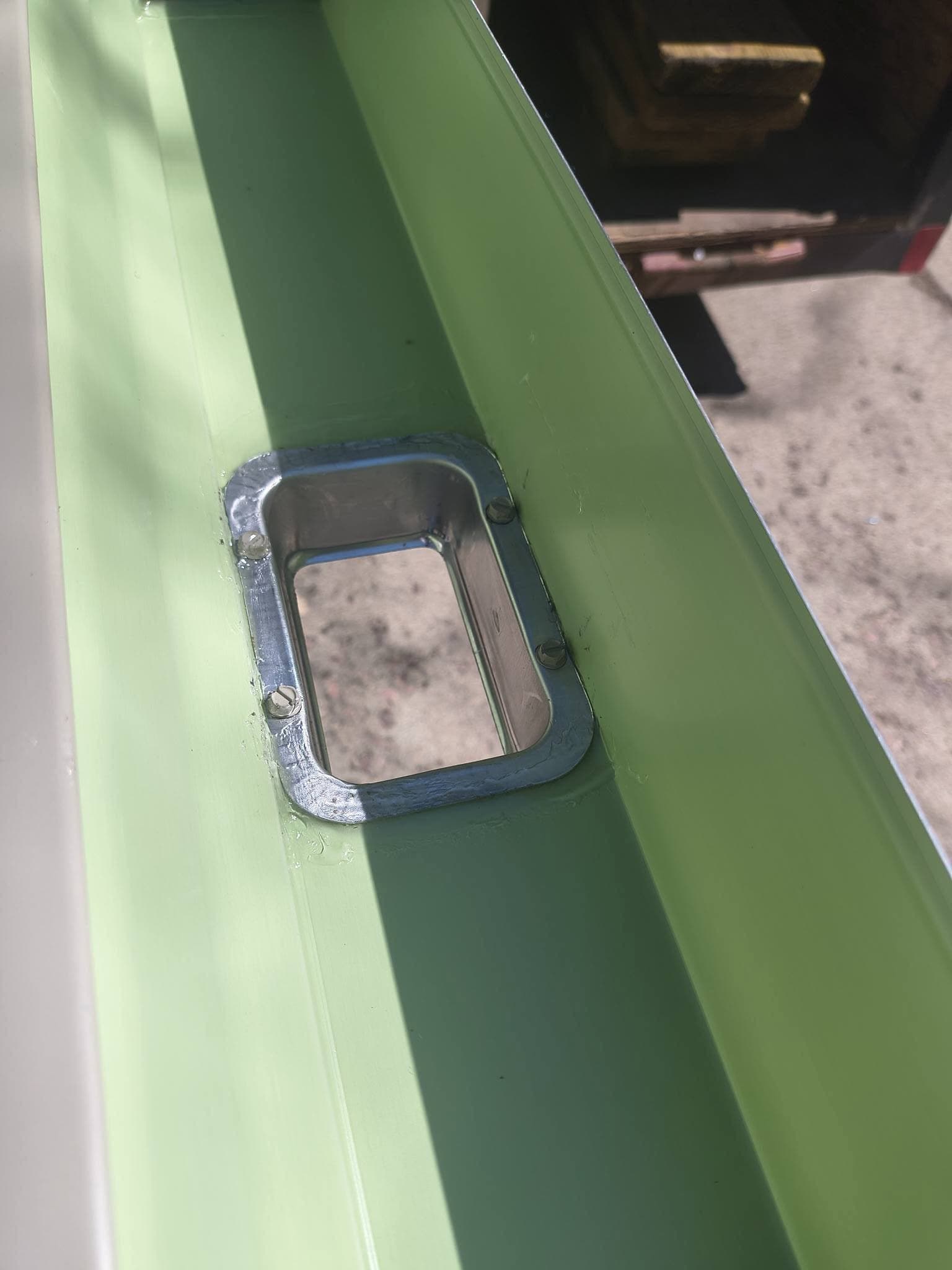 Downspout outlet cut into a green seamless gutter run, sealed and screwed