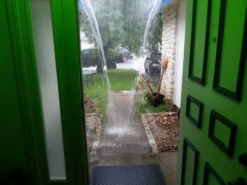 Rain sheeting off a porch roof past a green front door during a downpour