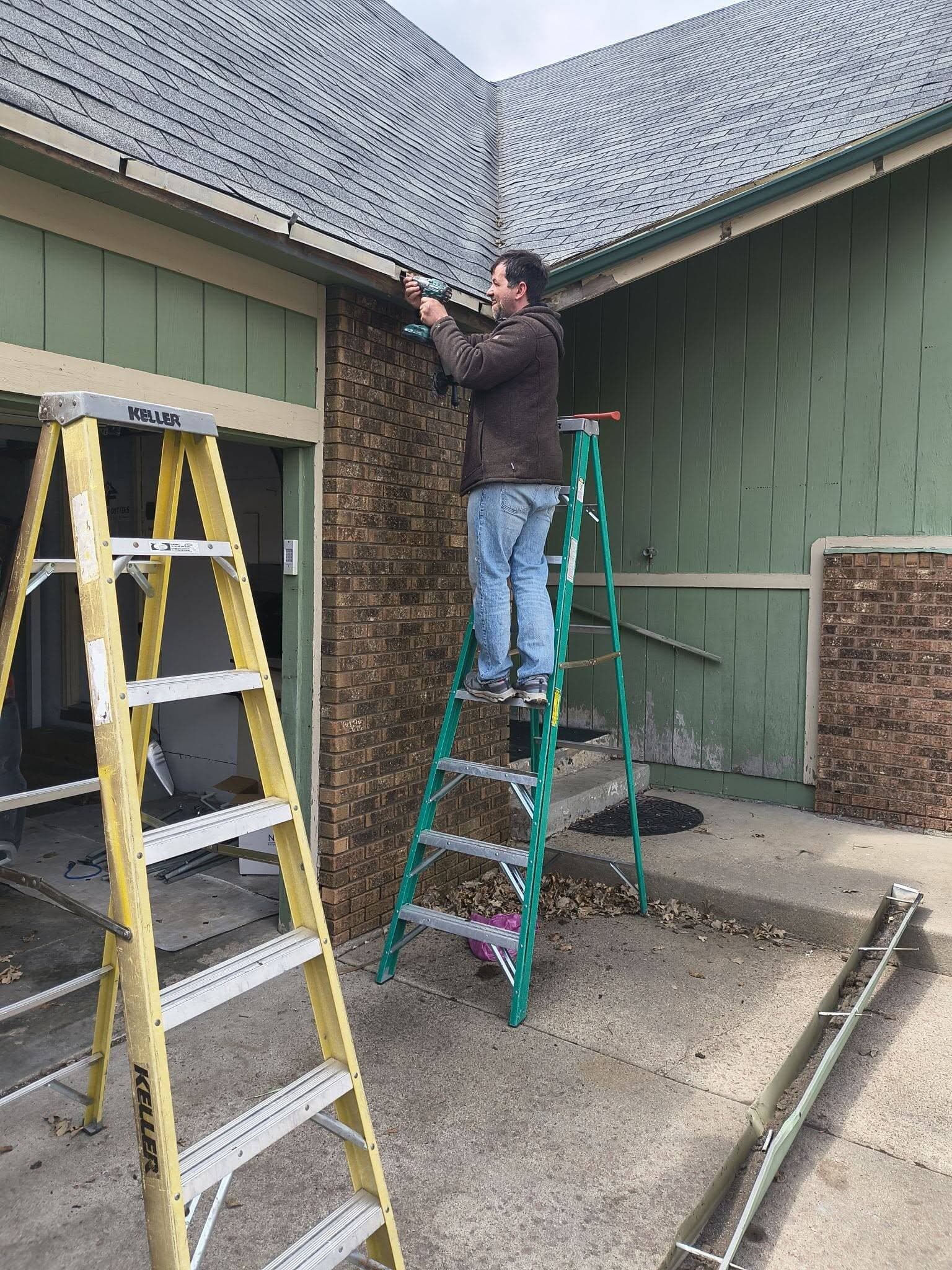 Worker on a ladder at the bare fascia with the old gutter taken down and lying on the driveway