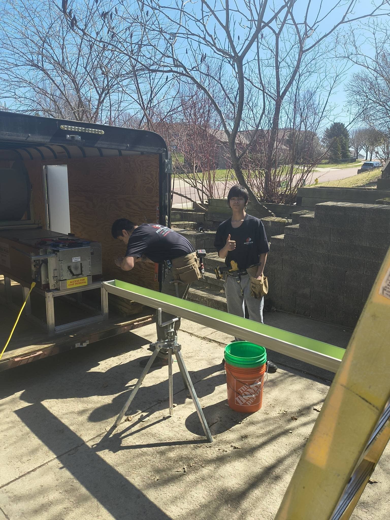 The seamless gutter machine in the trailer extruding a green run onto a stand in a driveway