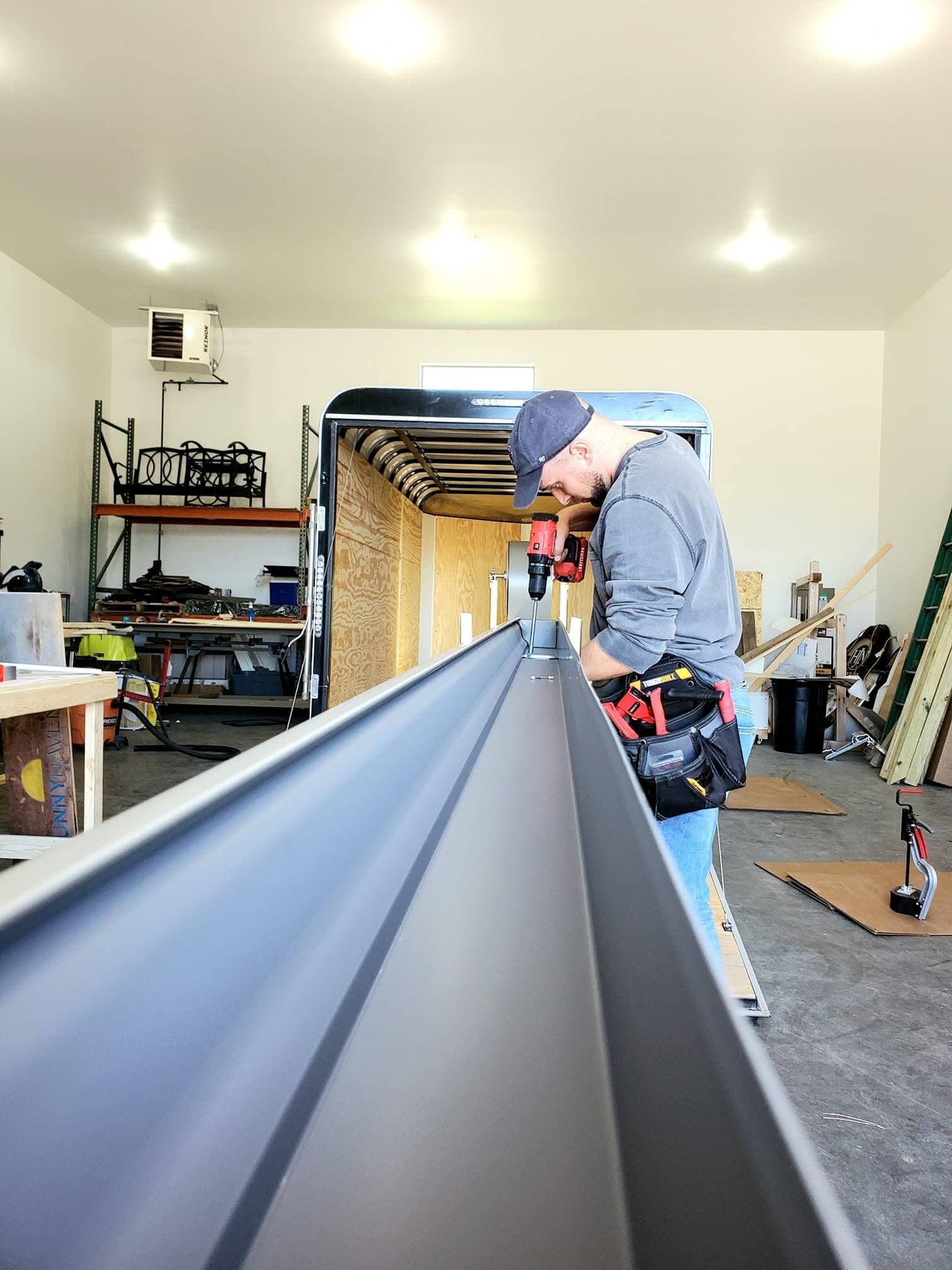 A dark charcoal gutter run coming off the seamless machine in the shop, worker fastening the end